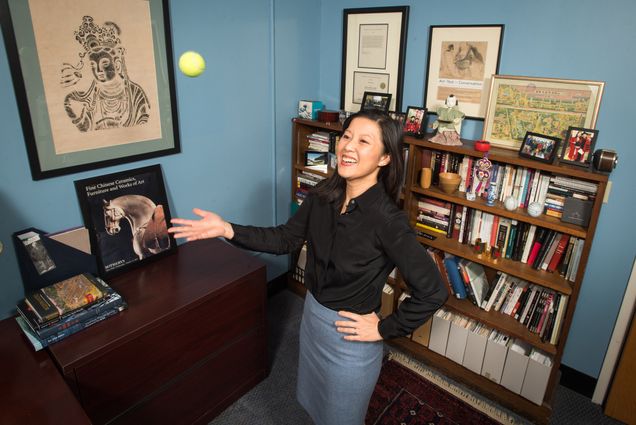A photo of Alice Tseng standing in her office throwing a tennis ball up in the air.