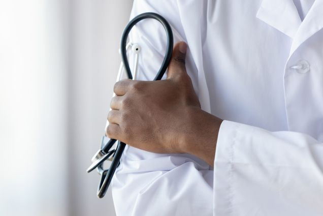 A photo of a doctor holding a stethoscope against their white lab coat.