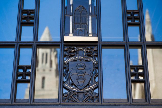 Photo of the entrance to STH with the BU Logo ("Boston University, Learning, Virtue, Piety") with the CAS tower reflected on the left and right.