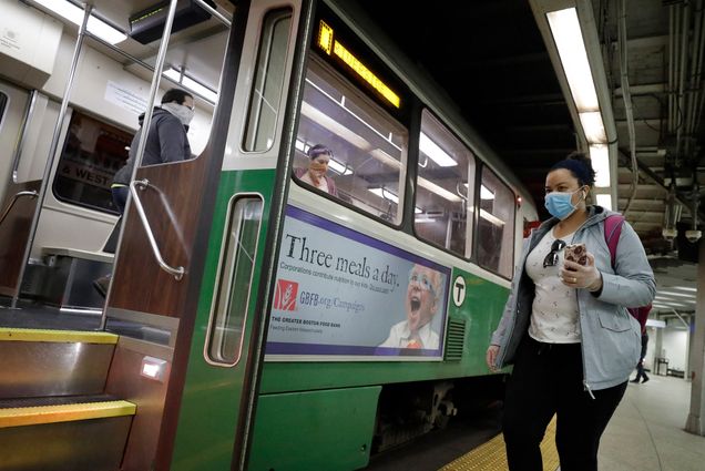 A photo of a woman in a mask holding her phone while she boards and MBTA green line train