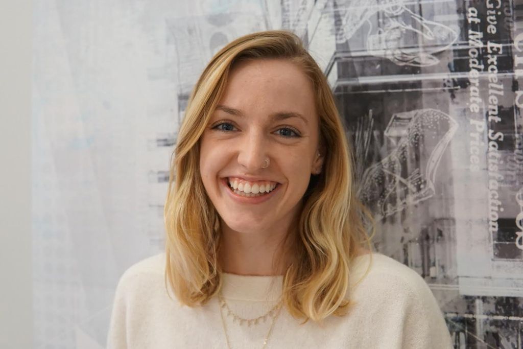 Portrait of Haley Cerretani (Sargent’20) in front of a wall collage. She wears a white sweater.