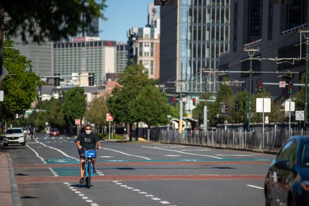 A photo of a man wearing a mask on a bicycle riding down an empty Commonwealth Ave.
