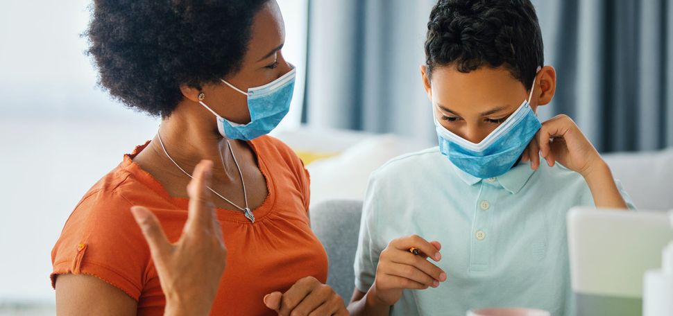 A photo of a woman and child working on schoolwork together at home while wearing masks