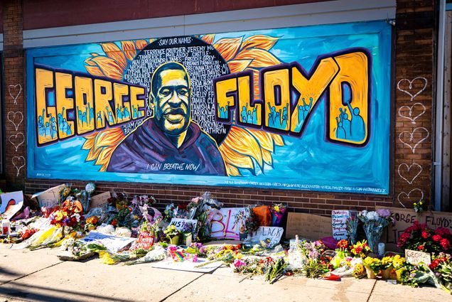 Brightly colored mural honoring George Floyd created during the Black Lives Matter protest in Minneapolis, Minnesota. The mural is a painting of Floyd with a sunflower behind him like a halo. "George Floyd" painted on either side of his portrait.