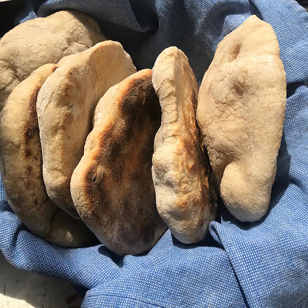 Photo of five homemade pitas in a basket with a light blue cloth.