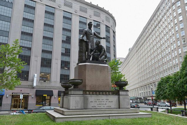 Photo of the Emancipation Statue in Park Square with Abraham Lincoln on May 21, 2013 in Boston, MA. The statue depicts Lincoln with his hadn extended as a man of color kneels at his feet. The buildings of Park Square and an overcast sky are seen in the background.
