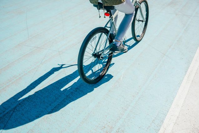 A photo of a person riding a bike that is casting a shadow onto the pavement they are riding on