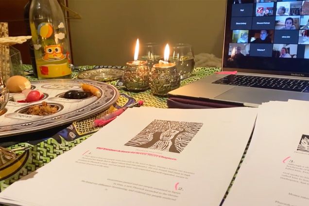 Photo of a computer, haggadah, and candles with a seder plate in the background. On the computer zoom call participants are seen.