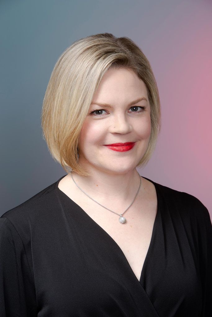Headshot of Erika Block (BUTI’96, CFA’02,’04) who smiles against a blue and pink backdrop.