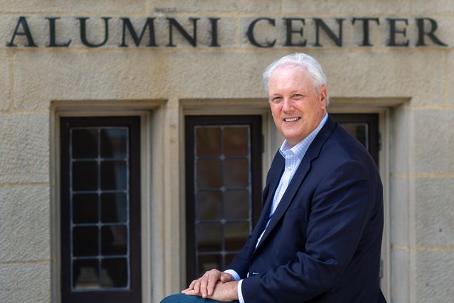 Steve Hall, VP in alumni relations who helped spearhead the hugely successful BU fund raising campaign, is retiring. Here he sits on one of the railings outside of the Dahod Family Alumni Center at the Castle on July 31, 2020. He wars a blue suits, and ornate windows are seen on the building behind hime with the sign "Dahod Family Alumni Center"