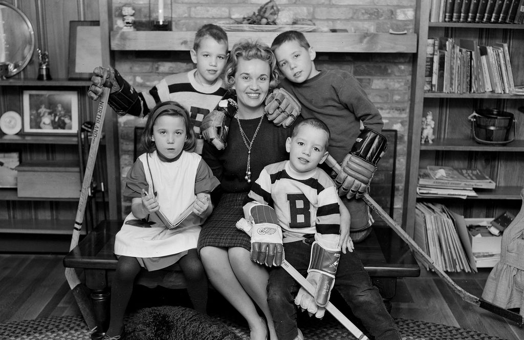 Black and white photo of the family of Boston University Hockey Coach Jack Kelley are photographed in their Walpole, Massachusetts home. Rear row David, Ginny and Paul. Front row: Nancy and Mark. The dog's name was not recorded. Two of the small boys wear BU jerseys and hold hockey sticks.