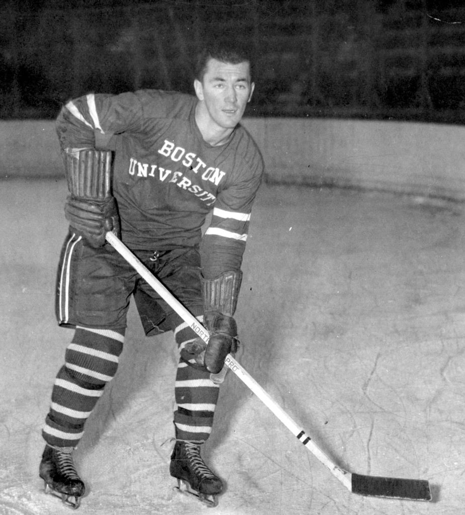 Black and white photo of Jack Kelley as a player on BU’s hockey team. He wears a Boston University jersey and holds a hockey stick.