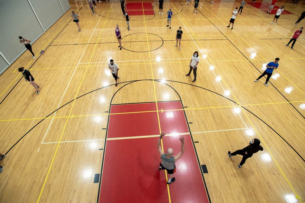 Photo of the gym in fitrec with people distanced very far apart. At the front, John O’Brien teaches a boxing course to roughly 40 students, all spaced out in 14-foot squares. The gym lights are reflected on the parquet floor.