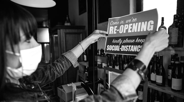 A photo of someone putting a reopening sign on the door of their business