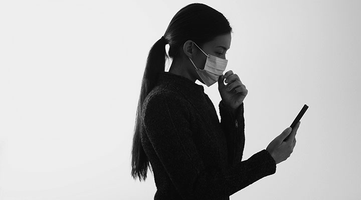 A photo of a woman in a mask looking at her smart phone
