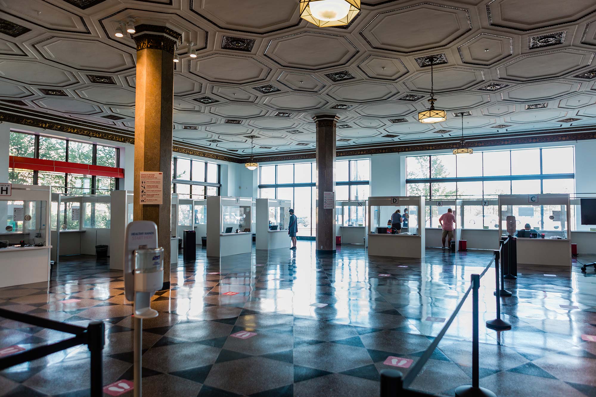 Photo of a Covid-19 collection site at 808 Commonwealth Ave. The floor is divided by black dividers and  white booths where people get tests are seen in the background.