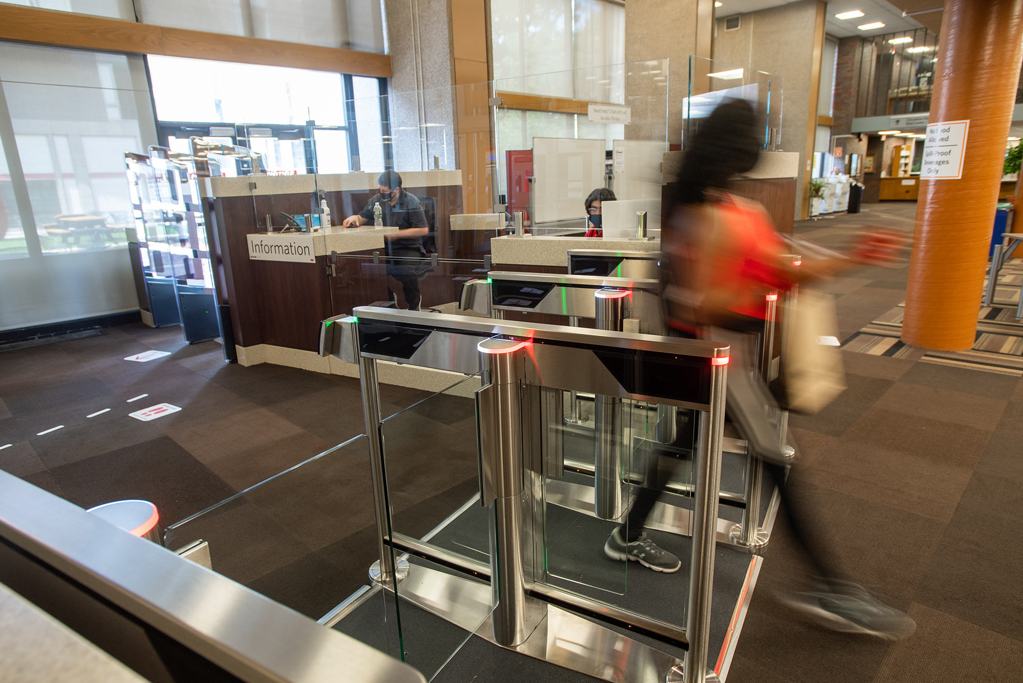 Photo of a student walking through the turnstiles at the entrance of Mugar Library.
