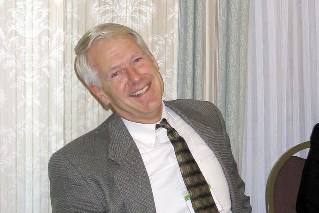Photo of William A. Anthony sitting in a chair in a suit and tie and smiling.
