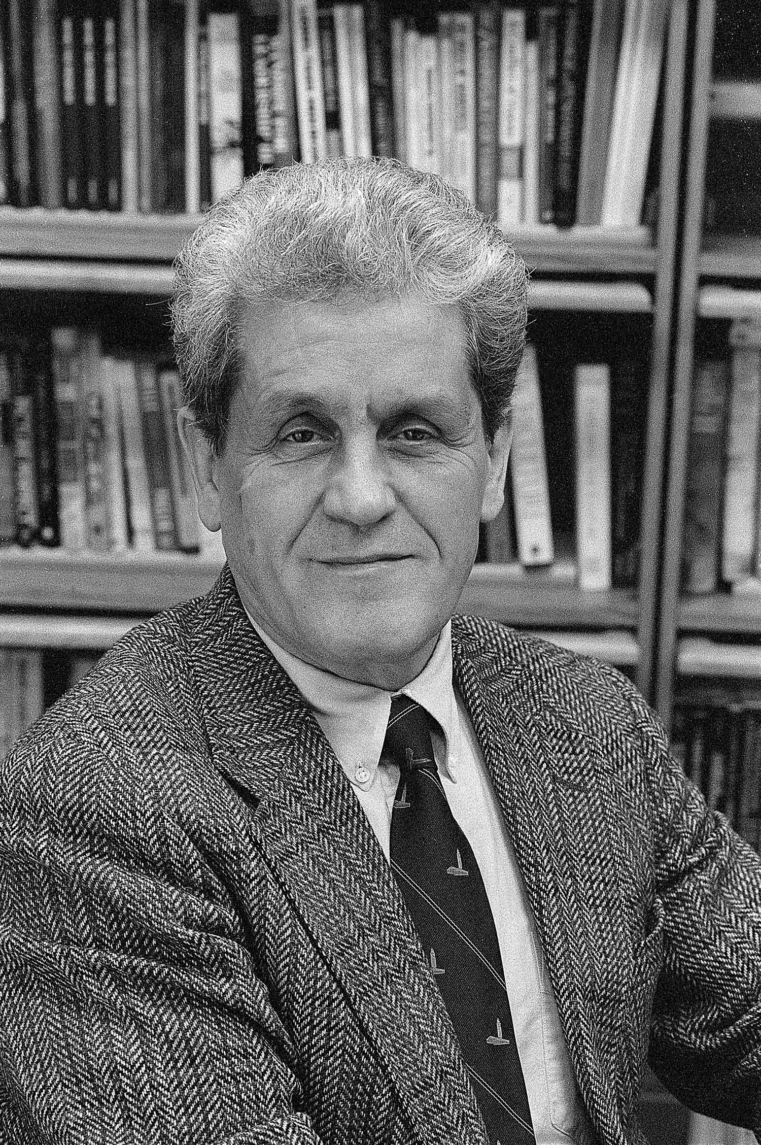 Black and white portrait of Joachim Maître in a checkered suit in front of a bookshelf.