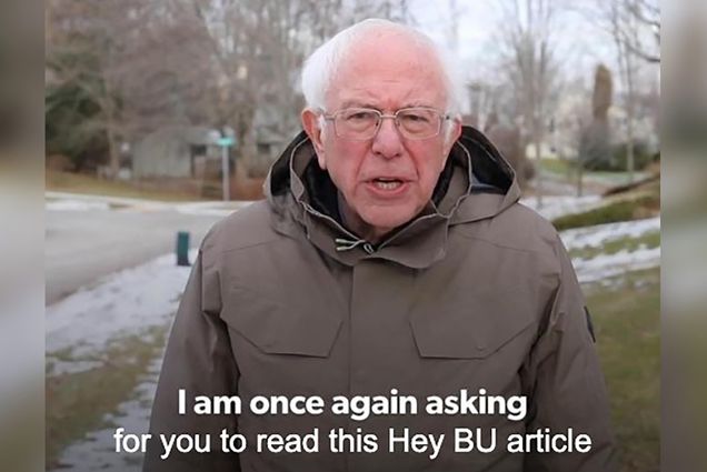 Screenshot of Bernie Sanders in a light brown rain coat from his iconic fundraising campaign video during the 2020 presidential primary. The closed captioning text reads “I am once again asking for you to read this Hey BU article.” Behind, a suburban neighborhood street corner is seen.