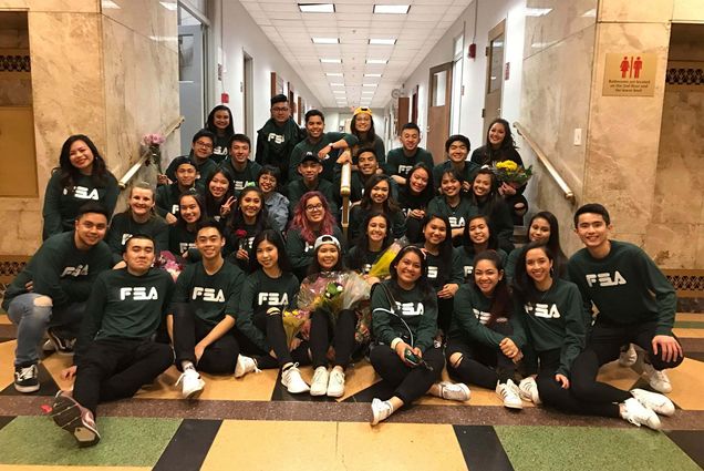 Photo of the students of the BU Filipino Student Association sitting in a hallway with green FSA sweatshirts on.
