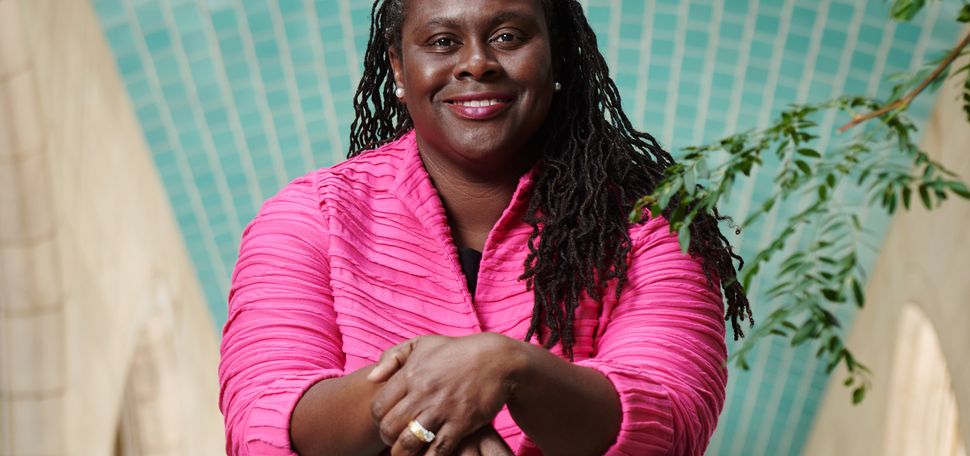 A portrait photo of Angela Onwuachi-Willig leaning against a railing with her hands crossed in front of her.