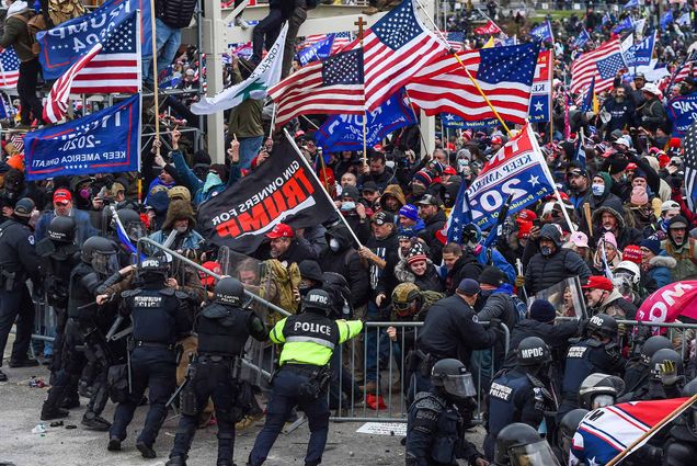 Photo of Trump supporters clashing with police and security forces as they storm the US Capitol in Washington, DC on January 6, 2021. Police officers, dressed in riot gear, push back a metal barrier as insurgent Trump supporters holding American flags and Trump 2020 flags try to break through the line.