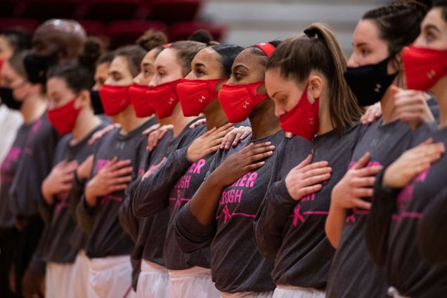 A photo of the BU women's basketball team wearing masks with their hands over their hearts before a game