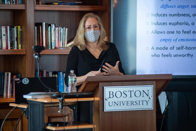 A photo of Paula Quatromoni teaching a class. She is wearing a mask while speaking at a podium.