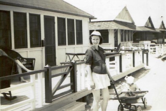Black and white photo of the author’s grandmother, Marie Moran, in Breezy Point, 1947. She wears a mid-thigh length skirt, hat, and pulls a wagon with a child in it.
