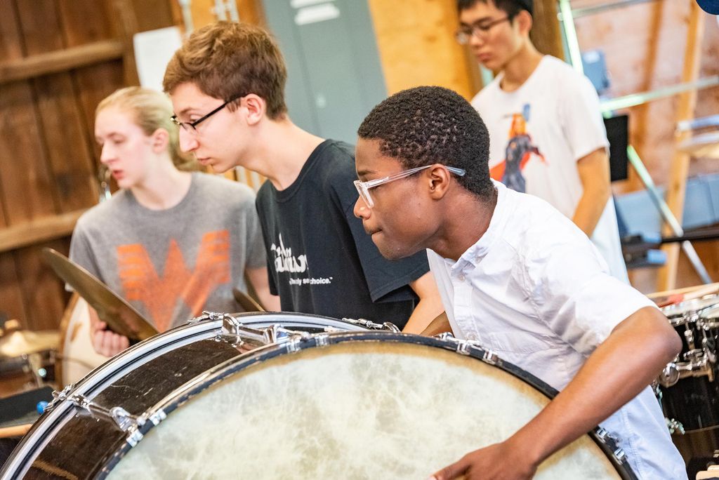 Photo of two young BUTI students playing, one plays a large drum, others in the background play the cymbals.