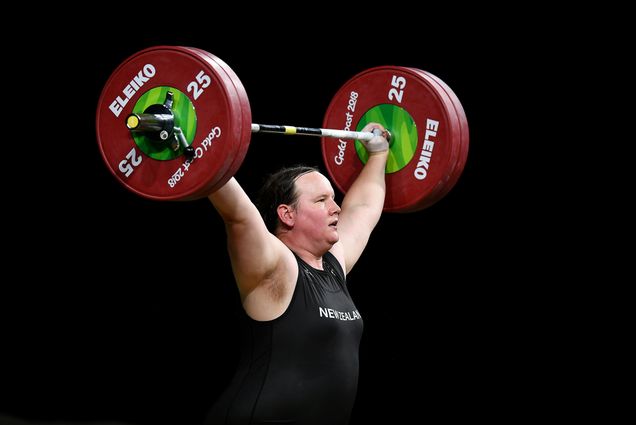 Photo of Laurel Hubbard of New Zealand as she competes in the women’s +90kg weightlifting final on April 9, 2018 at the Commonwealth Games in Gold Coast, Australia. She wears a black body suit and lifts a large barbell with green and red weights over her head. Photo by Dan Mullan/Getty Images