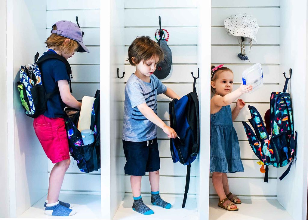 3 school children packing their backpacks in cubbies.