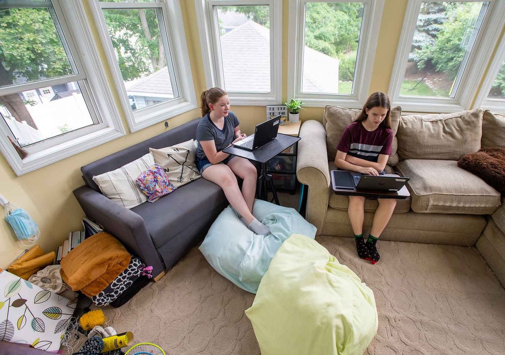 2 children attending class on their laptops remote learning in their living room.