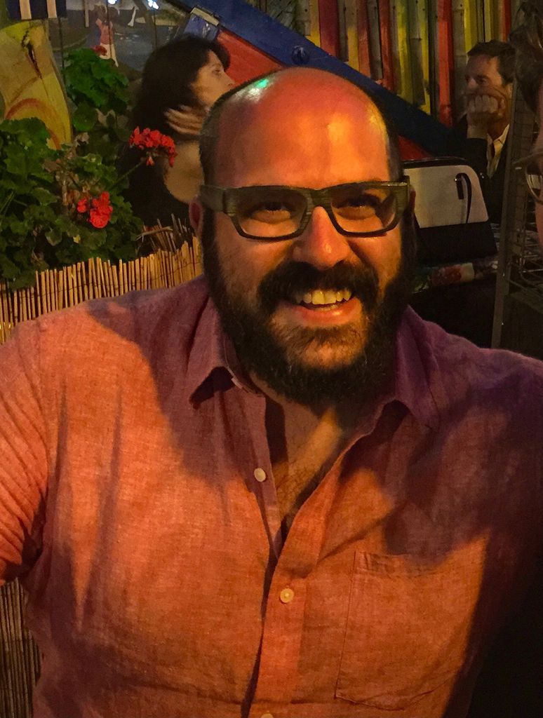 Photo of Justin Bias in a pink shirt; he smiles wide and appears to be out to eat.
