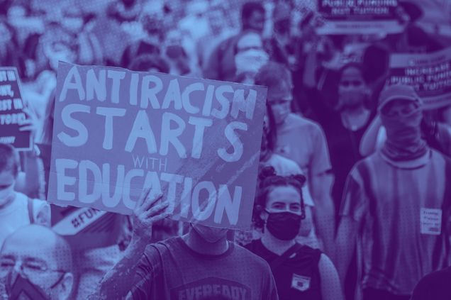 A crowd of people marching at a Black Lives Matter protest. A man holds a sign that says "Antiracism starts with education" at the front of the crowd.