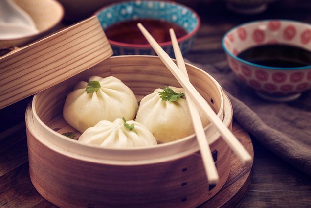 Photo of three dumplings in a steamer basket with a pair of chopsticks resting on the edge of the steamer.