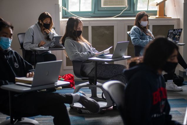 Photo of Emily Chua’s class WR120 K8 Planet Ocean, a first-year writing seminar focused on ocean science in CAS September 22, 2020. Students sit in rolling desks and look at their laptops; many of them wear sweatshirts and all of them wear facemasks in the dimly lit classroom.