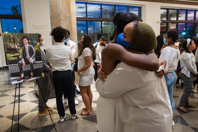 Photo of Beverly Bruno (SAR’22), president of Minority Connection Initiative and Malika Kounkourou (CAS’22), with the blue mask, embracing at a gathering in remembrance of Kendall Castañeda (CAS'21), who died on August 22. A photo of Castañeda is seen on an easel at left. Other students are seen behind the friends.