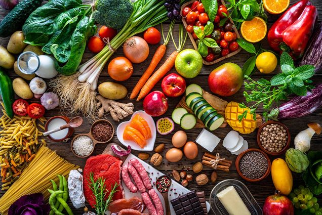 Aerial photo of a rustic table filled with fruits, vegetables, pasta, milk, nuts, and more.