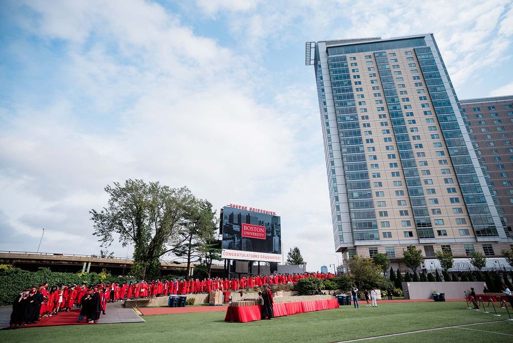 View of Nickerson Field with Student Village 2 dorm building in the background as BU Class of 2020 graduating students walk onto the field for Commencement.