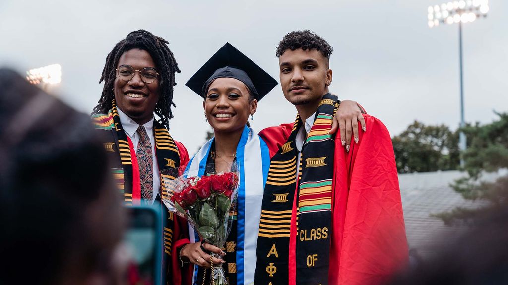 Three Black students pose for a celebratory photo following their Commencement ceremony on Nickerson Field.