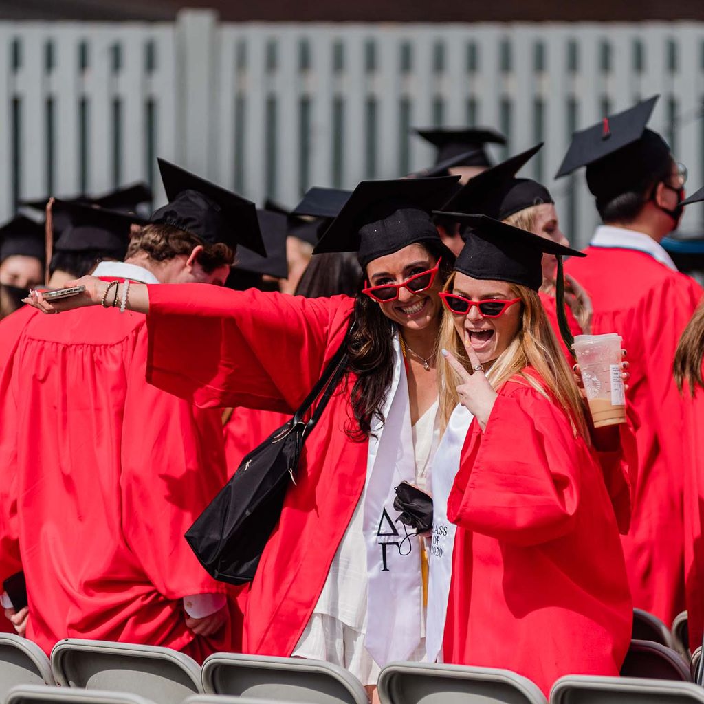 Two BU Class of 2020 graduates wearing red sunglasses pose for a photo during Commencement.