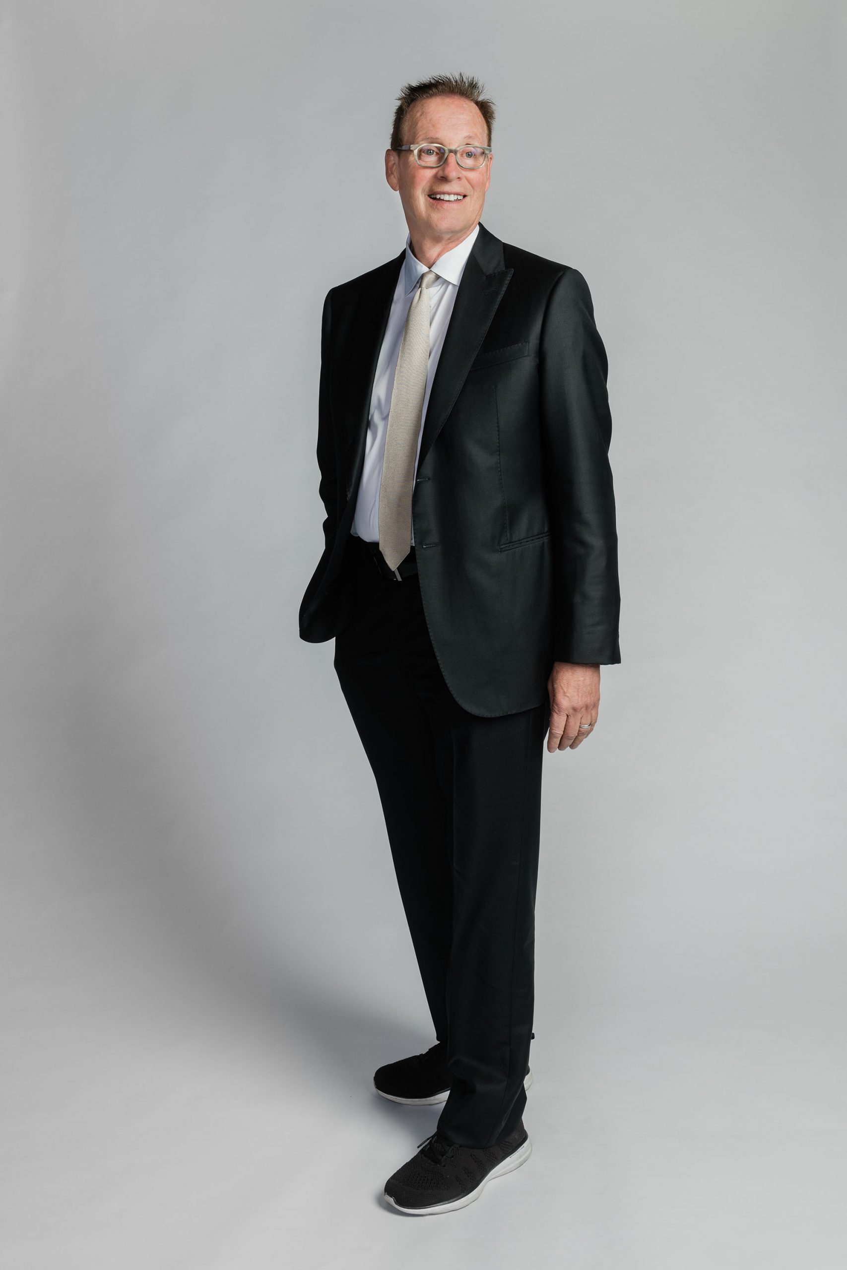 a studio photo of Boston University's Board of Trustees member Richard C. Shipley. He looks to the distance wearing a black suit in front of a grey background.