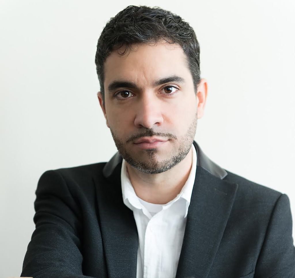 headshot of Dariel Suarez . He looks straight at the camera wearing a white collared shirt and black blazer in front of a white background.