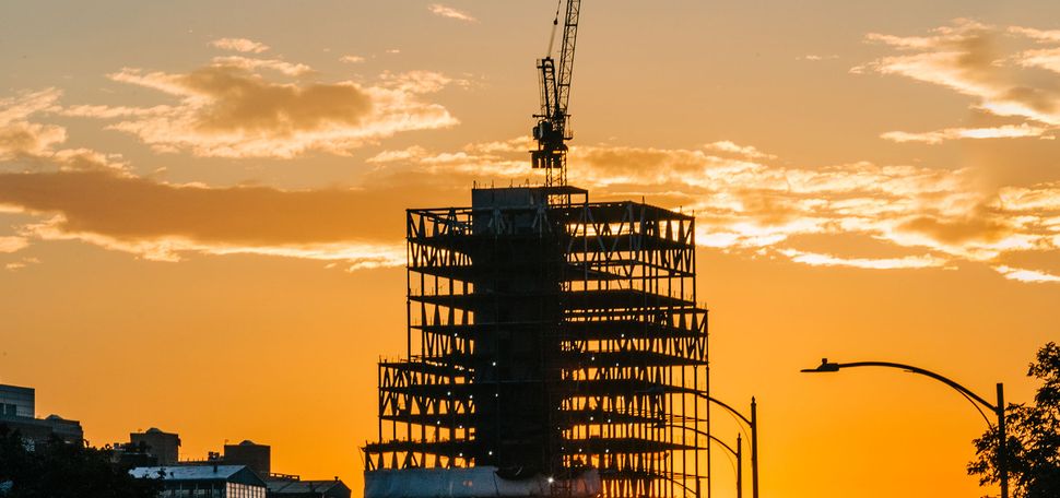 photo of BU’s new 19-story Center for Computing & Data Sciences during construction. A crane is atop the structure. It serves as a looming figure during a scenic orange sunset. Cars are seen in the horizon.
