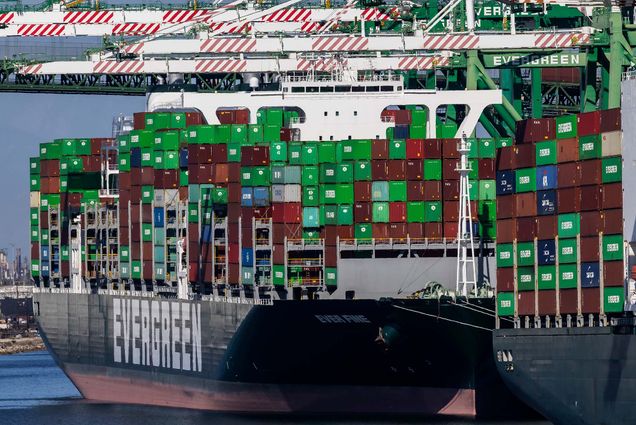 Photo representative of the supply chain crisis 2021: A large, Evergreen shipping container docked in the Port of Los Angeles. Green, red, and blue shipping containers are piled high on the ships, as they wait to be unloaded during a worker shortage.