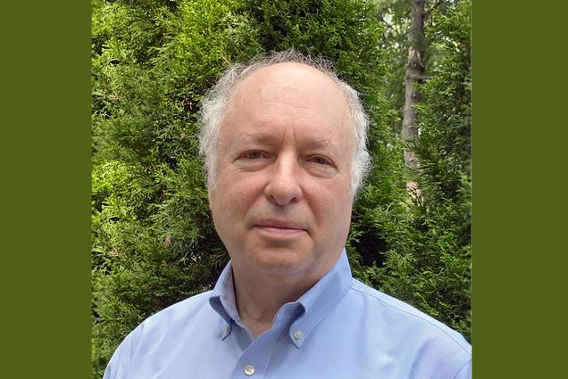 headshot of Greg Blonder, visiting scholar and former professor of the practice in mechanical engineering at BU’s College of Engineering. He smiles as he looks to the camera wearing a light blue collared shirt. Background is full of trees and greenery.