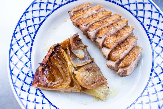 Photo of a sliced Duck Breast and Onion Tarte Tatin on a white plate with a blue border.