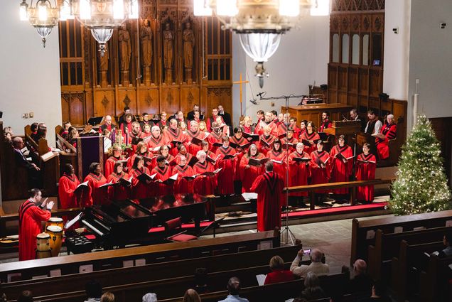 photo of the 45th Annual Service of Lessons and Carols on December 10, 2018 at Boston University's Marsh Chapel. The carolers are dressed in red robes and stand singing with black librettos open.